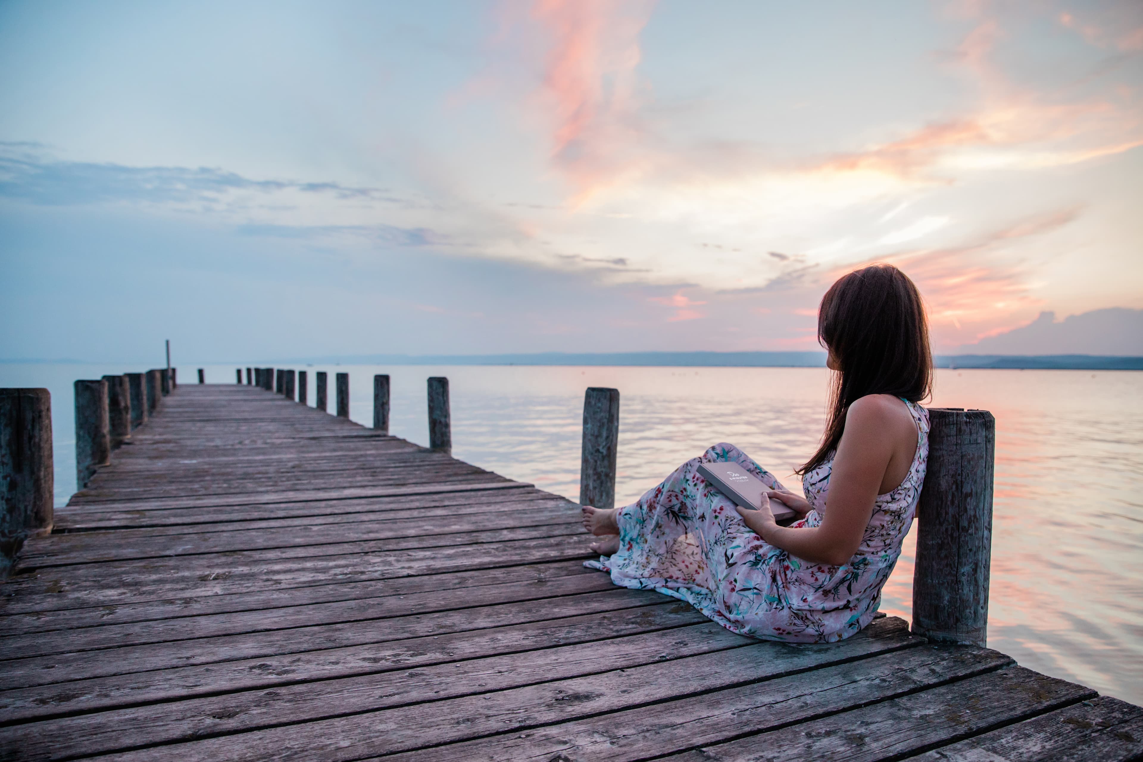 Angelika sitzt mit einem Buch auf einem Steg bei Sonnenuntergang
